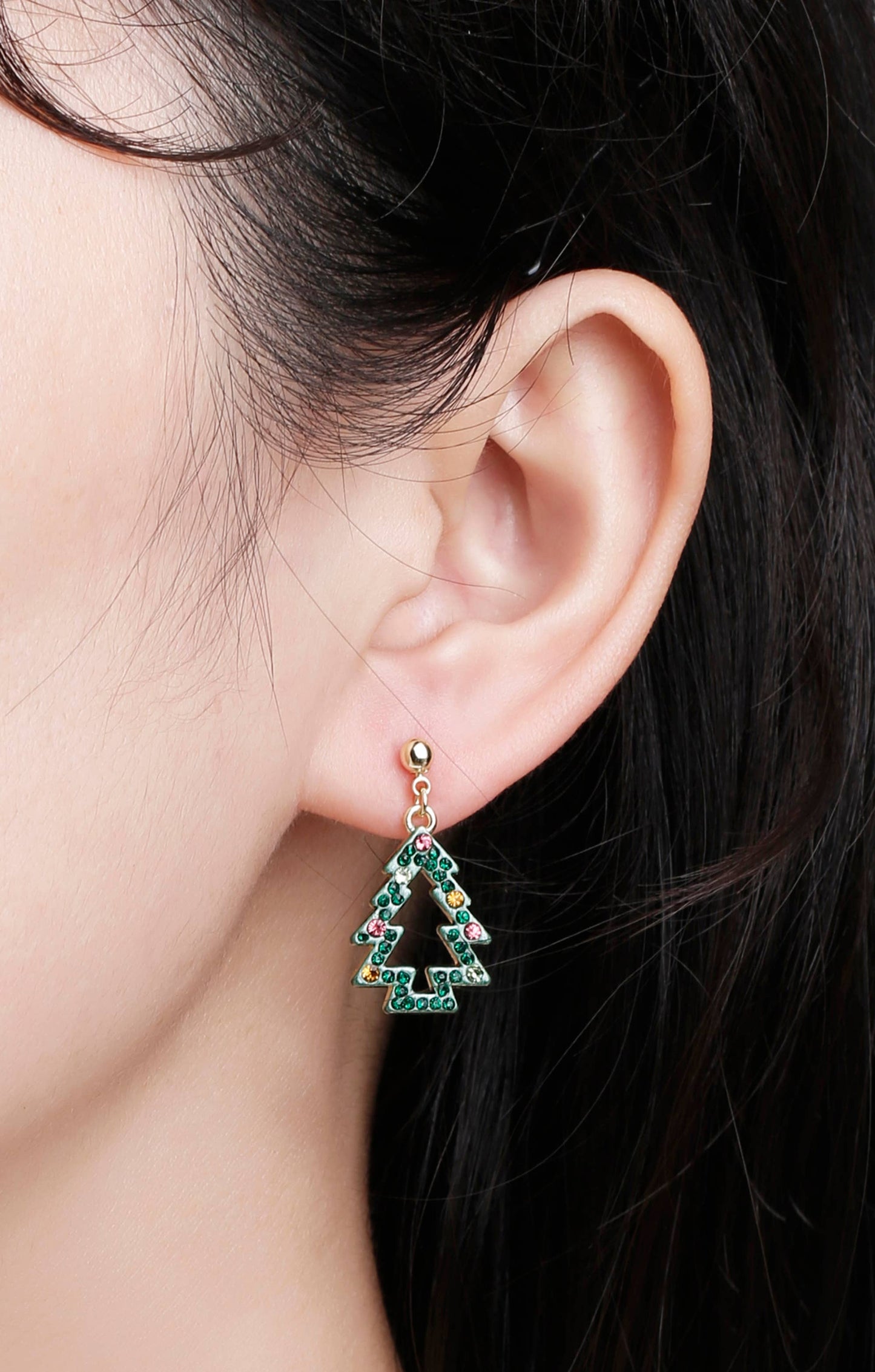 Close-up of girl wearing festive Christmas tree earrings with green crystals and colorful stones, gold-tone ball stud
