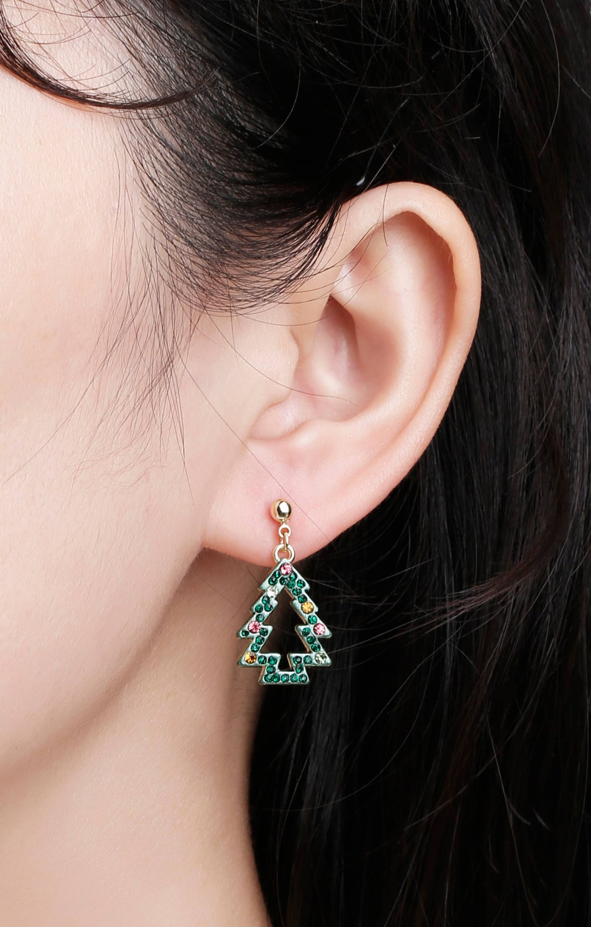 Close-up of girl wearing festive Christmas tree earrings with green crystals and colorful stones, gold-tone ball stud
