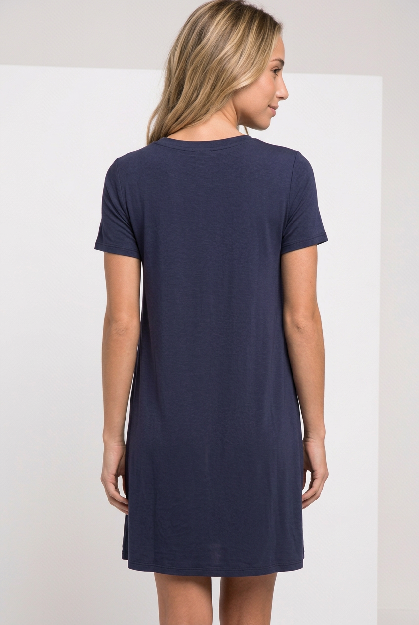 Back view of navy short-sleeve T-shirt swing dress with a plain high round neckline, worn by a blonde model looking over her shoulder.