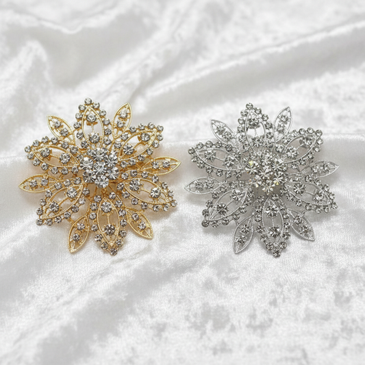 Gold-tone and silver-tone 63mm rhinestone flower brooches with brilliant clear crystals displayed on white velvet, premium jewelry photography showing both color variations