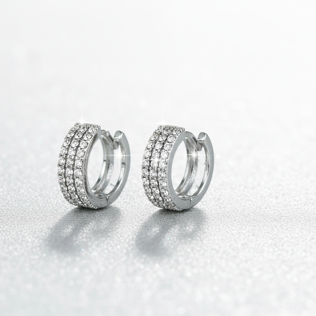 Premium hero banner featuring pair of silver huggie hoop earrings with three rows of CZ rhinestones on front half and smooth silver metal on back, 1/2-inch petite hoops displayed against luxurious gradient background