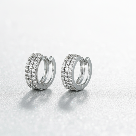 Premium hero banner featuring pair of silver huggie hoop earrings with three rows of CZ rhinestones on front half and smooth silver metal on back, 1/2-inch petite hoops displayed against luxurious gradient background