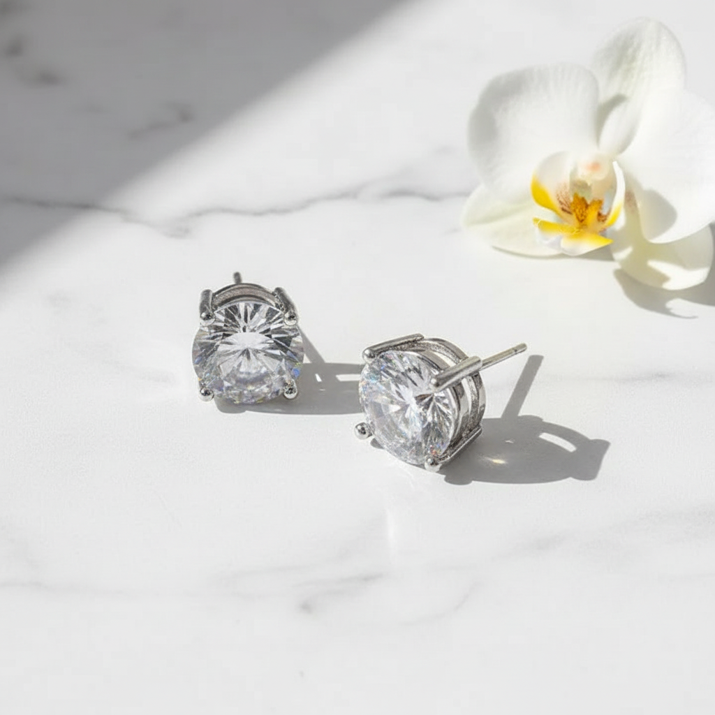 Large silver cubic zirconia stud earrings on white marble surface with white orchid bloom accent