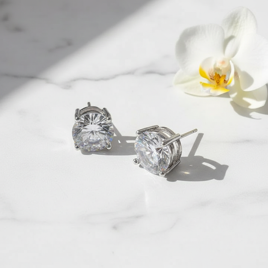 Large silver cubic zirconia stud earrings on white marble surface with white orchid bloom accent