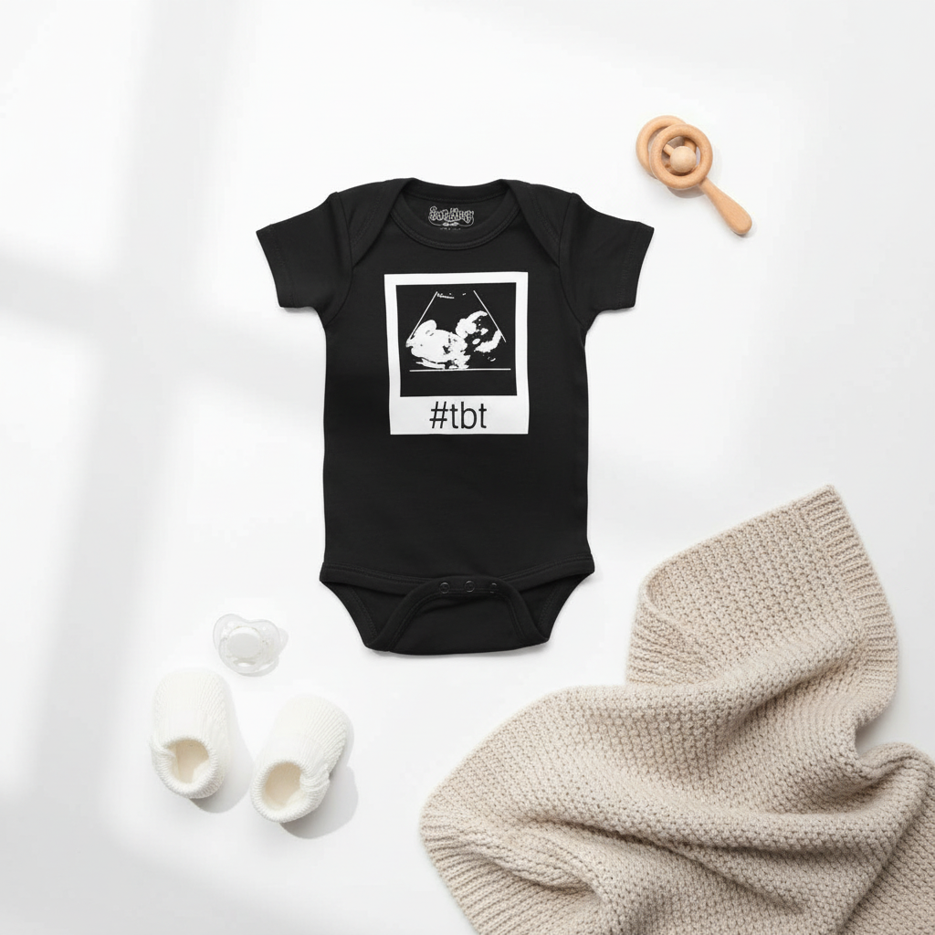 Black baby onesie with sonogram ultrasound image and #TBT text, styled with wooden toys and neutral baby accessories on white background