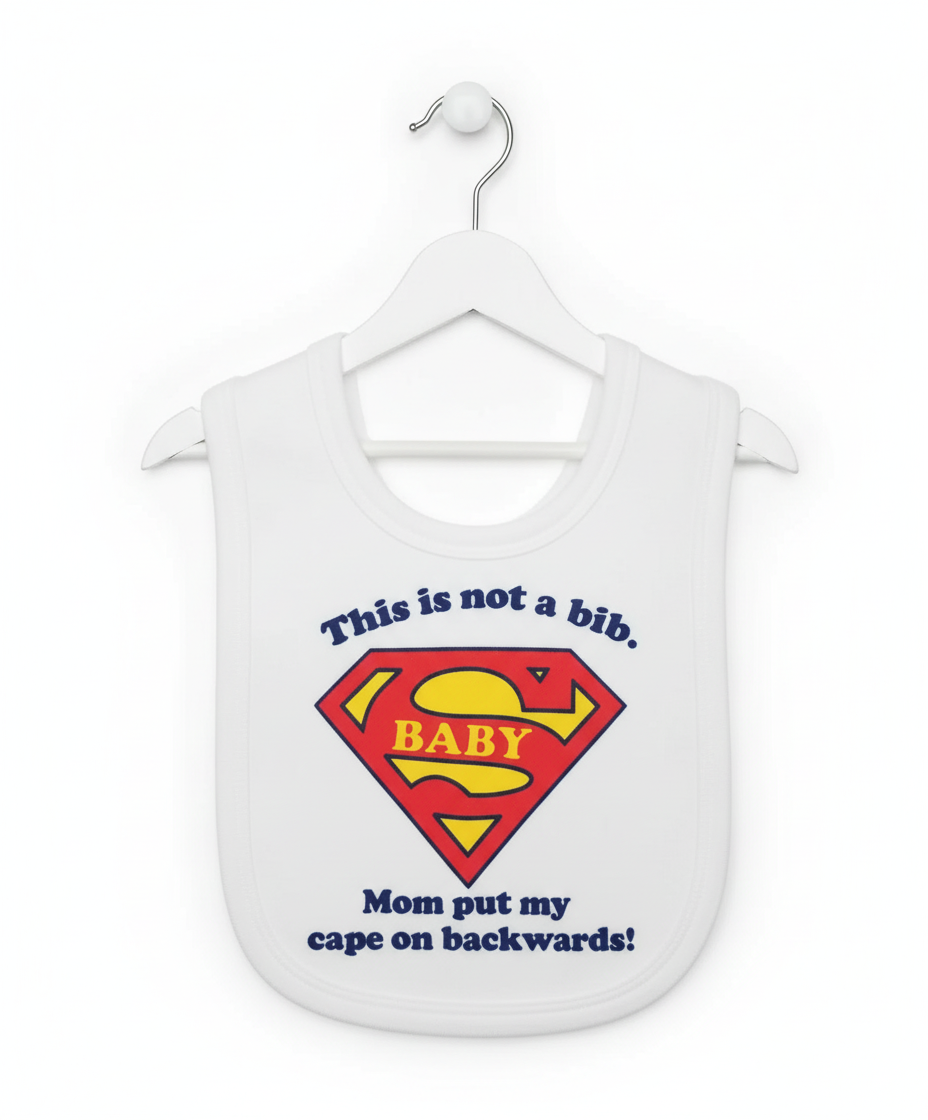 White baby bib with red and yellow Superman BABY shield and 'This is not a bib Mom put my cape on backwards' text hanging on white hanger