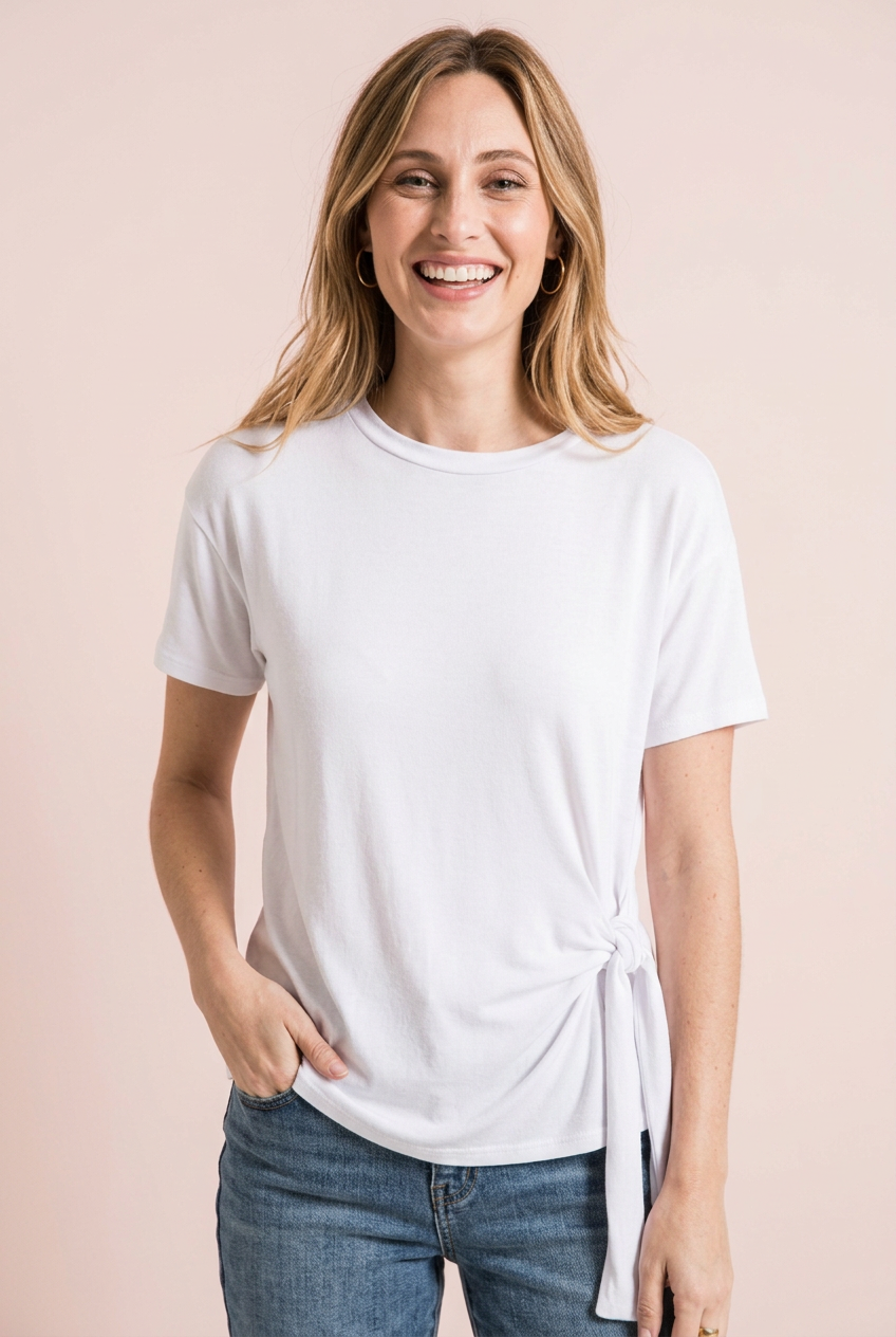 Front view of a woman wearing a white side-tie crewneck tee and blue jeans.
