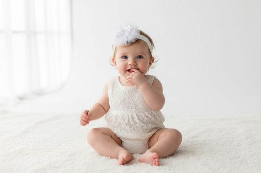 Baby girl wearing white tulle flower headband with 5-inch rhinestone bow in professional studio portrait with natural window light on white backdrop