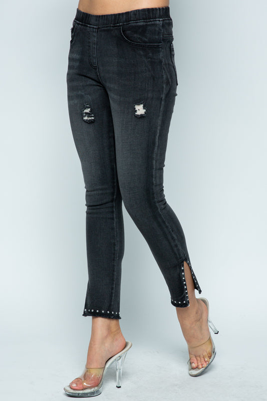 Woman wearing dark wash denim jeggings with distressed details, studded hem and ankle slit detail, front view